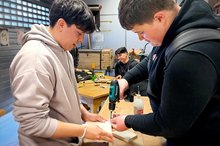 Zwei Auszubildende arbeiten an einer Holz-Werkbank.